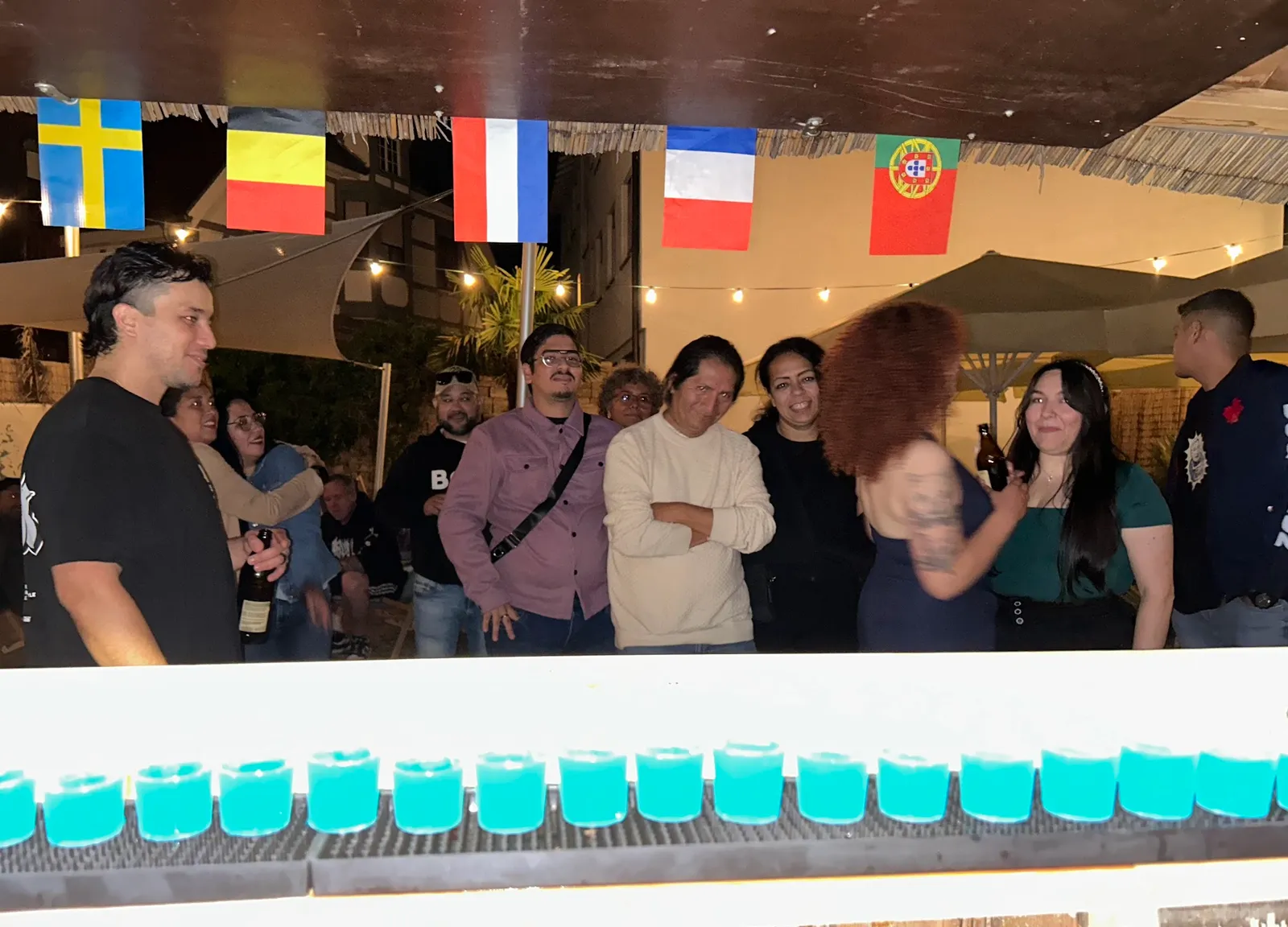 Lange Reihe blau leuchtender Shots auf der Theke bei Nacht mit feiernden Gästen